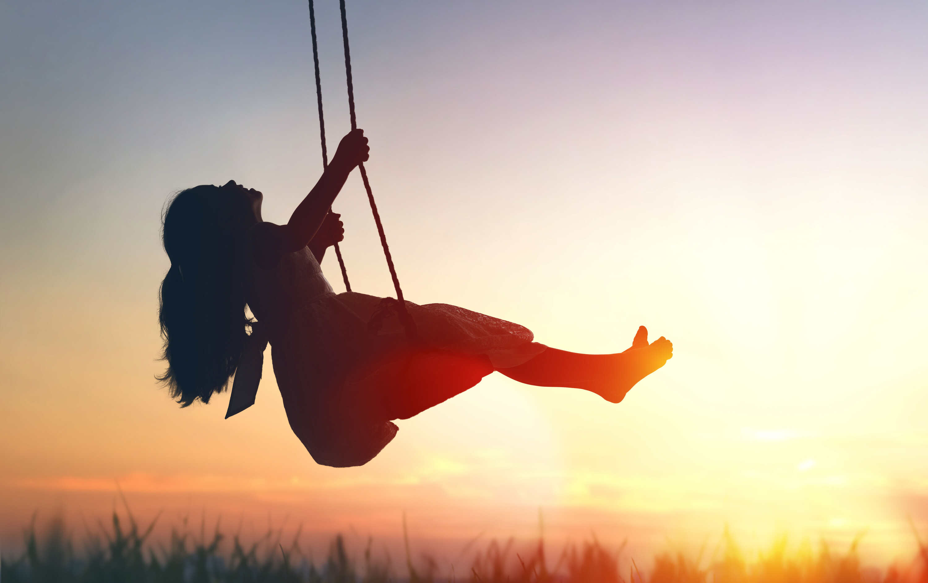 Bild zeigt ein Mädchen, das bei Sonnenuntergang auf einer Schaukel sitzt.